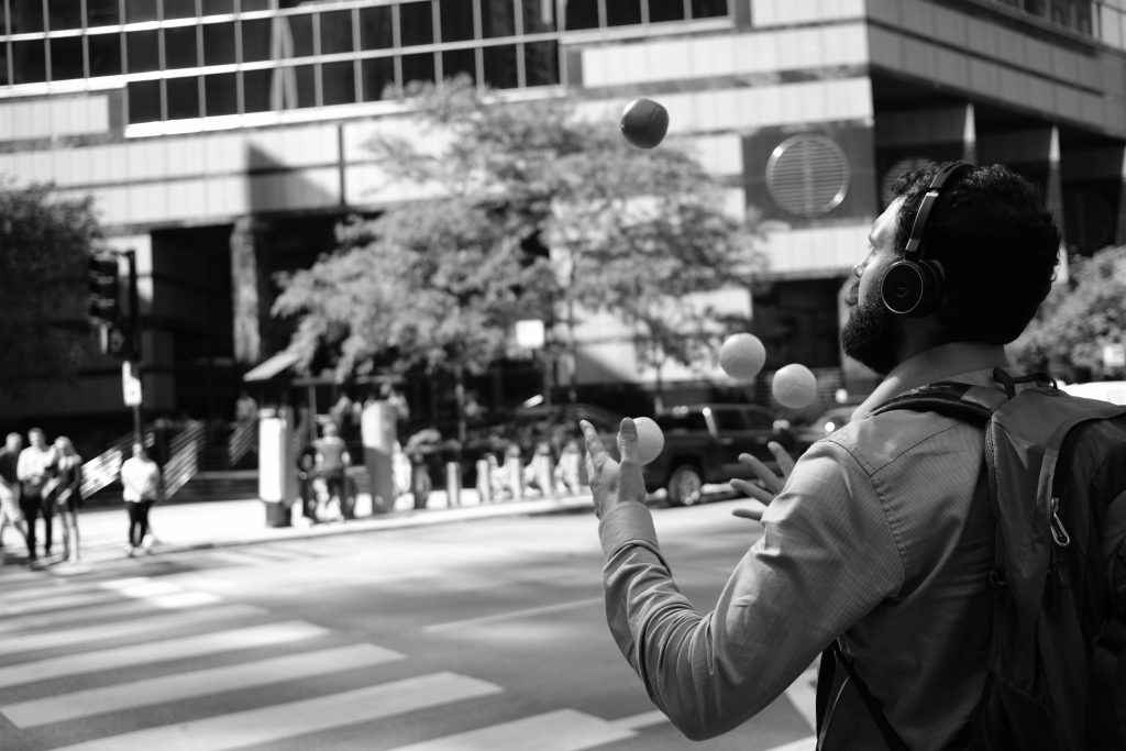 Photo by Matt Bero on Unsplash
Photo of a business person with headset on, a backpack, wearing a shirt, crossing a zebra pad juggling some balls